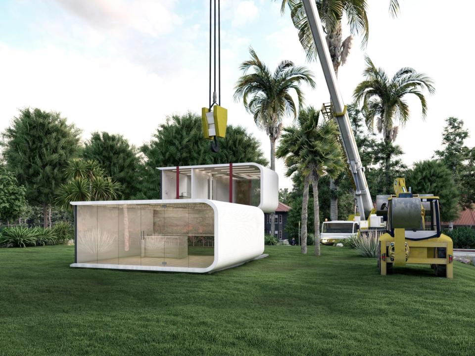 The ADU in a backyard on a patch of grass with palm trees. There's a crane in the back