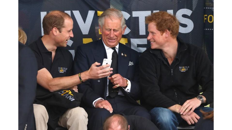 Prince William, Duke of Cambridge, Prince Charles, Prince of Wales & Prince Harry look at a mobile phone as they watch the athletics during the Invictus Games