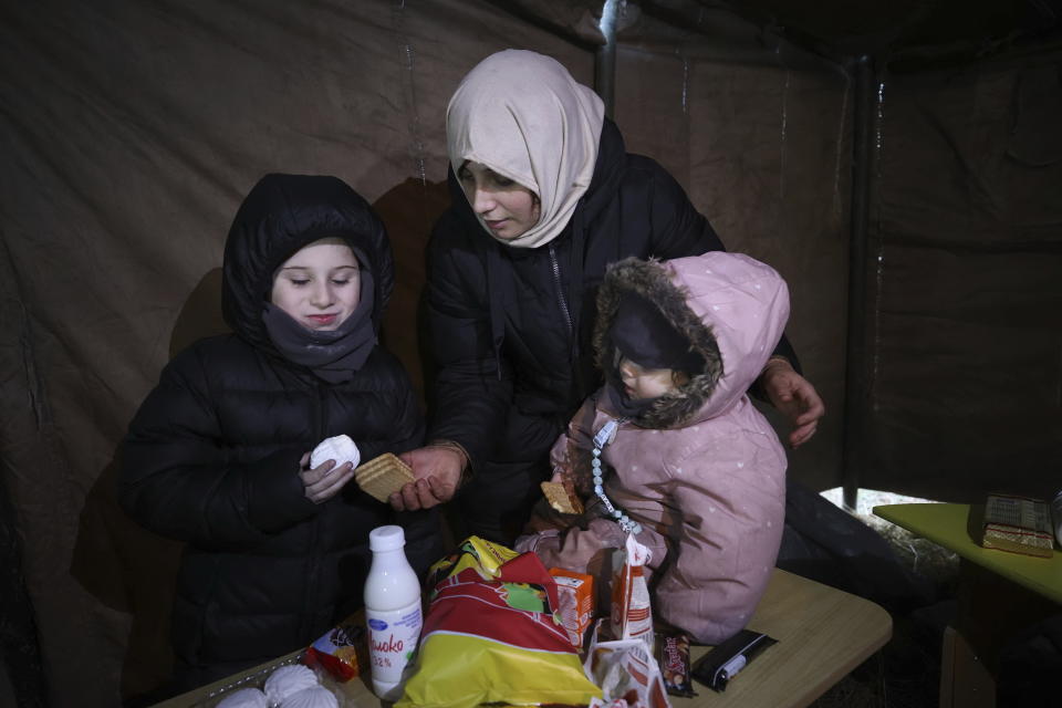 Migrant family receive food delivered by Belarusian volunteers as they gather at the Belarus-Poland border near Grodno, Belarus, Saturday, Nov. 13, 2021. A large number of migrants are in a makeshift camp on the Belarusian side of the border in frigid conditions. Belarusian state news agency Belta reported that Lukashenko on Saturday ordered the military to set up tents at the border where food and other humanitarian aid can be gathered and distributed to the migrants. (Leonid Shcheglov/BelTA pool photo via AP)