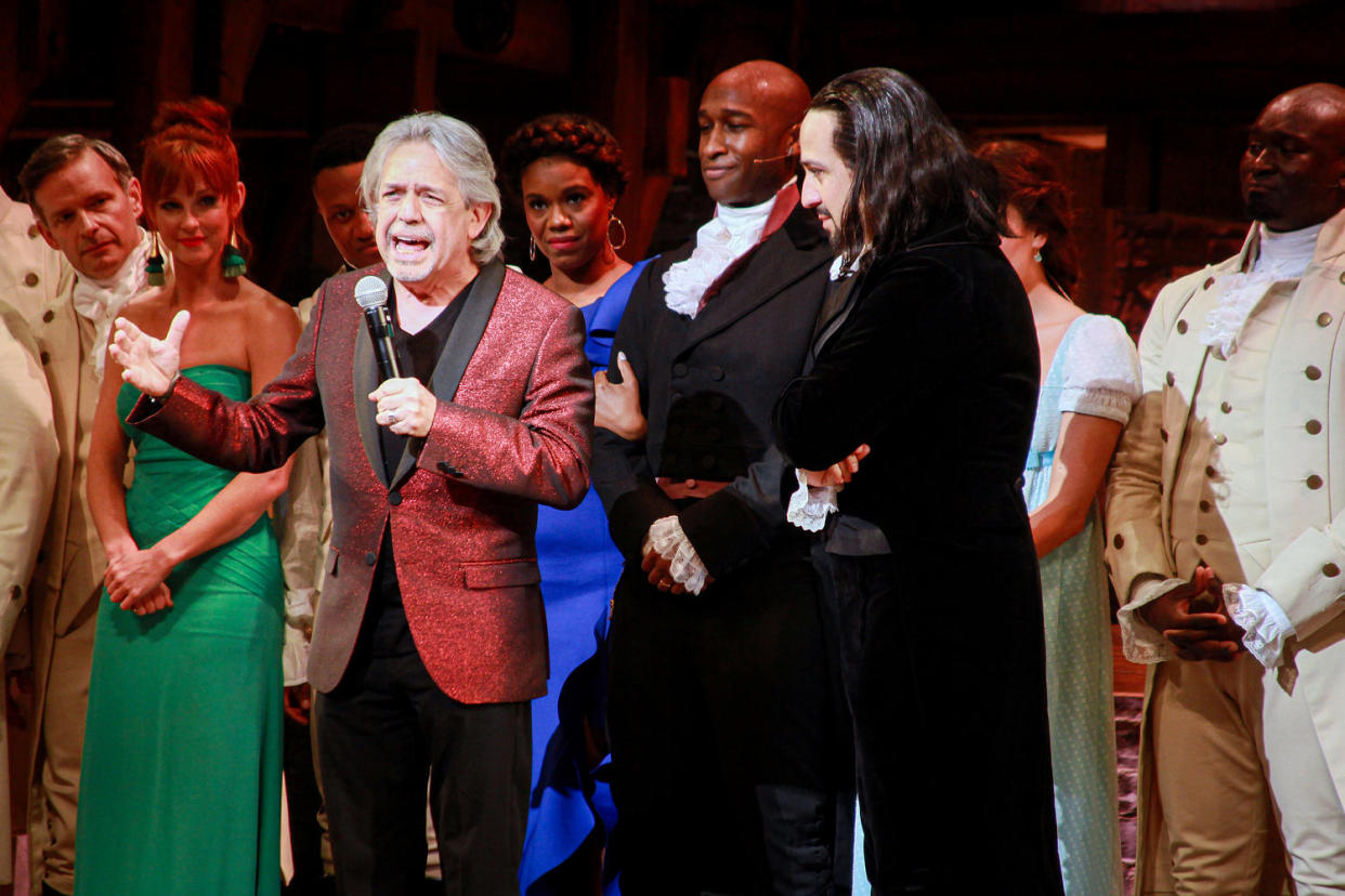 Luis Miranda speaks while Lin-Manuel Miranda and the cast of Hamilton stand on stage. (Gladys Vega / Getty Images for 