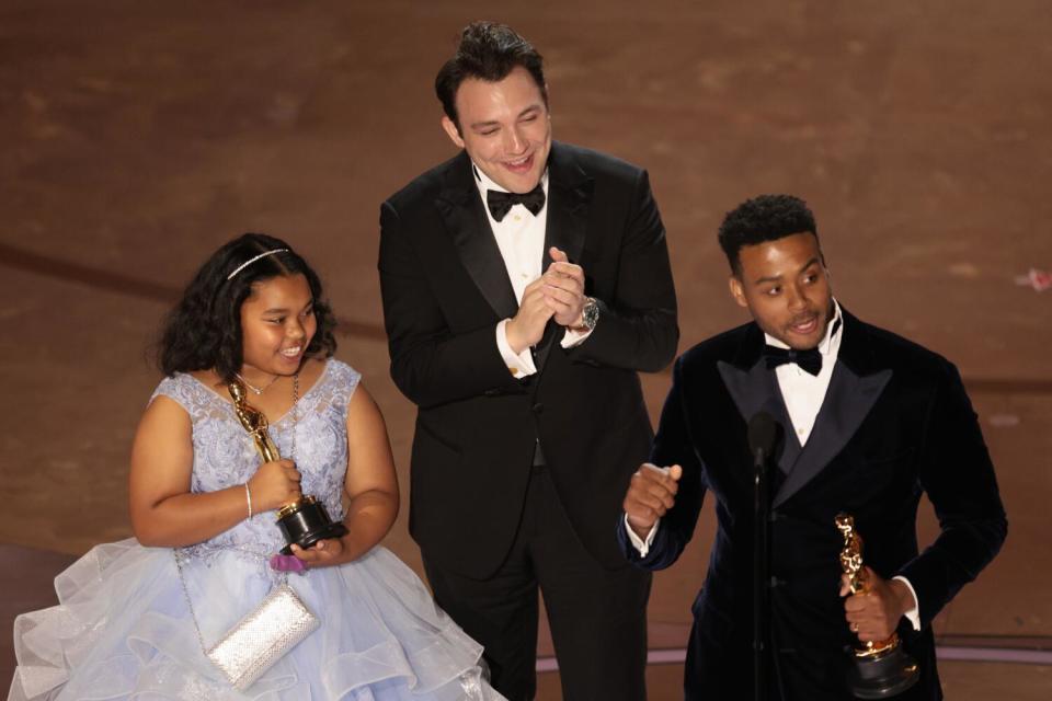 A girl in a dress and two men onstage.