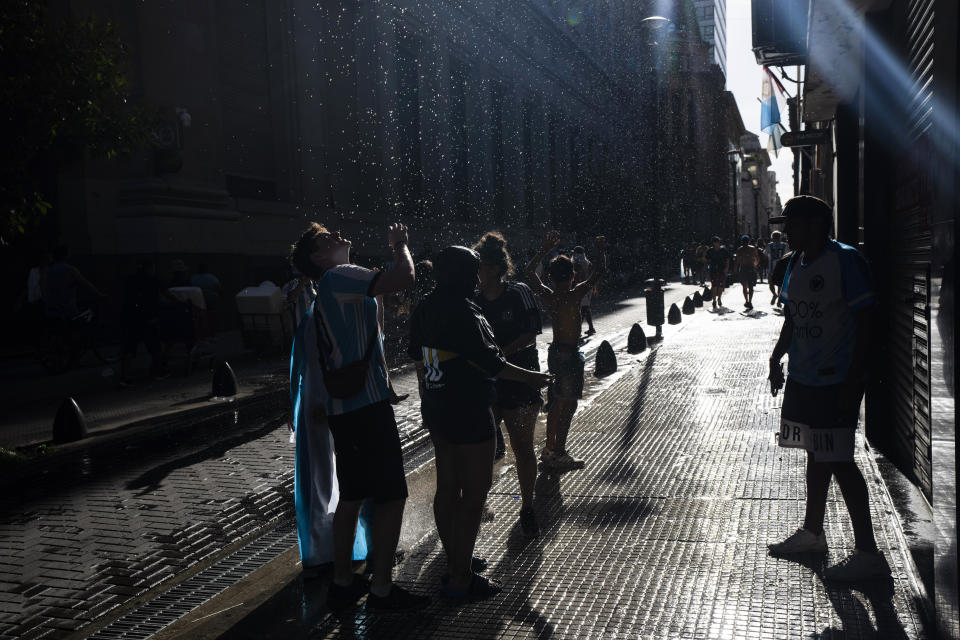 Soccer fans refresh themselves with water that falls from a broken pipe, after waiting for hours for a homecoming parade for the players who won the World Cup title, in Buenos Aires, Argentina, Tuesday, Dec. 20, 2022. A parade to celebrate the Argentine World Cup champions was abruptly cut short Tuesday as millions of people poured onto thoroughfares, highways and overpasses in a chaotic attempt to catch a glimpse of the national team. (AP Photo/Rodrigo Abd)