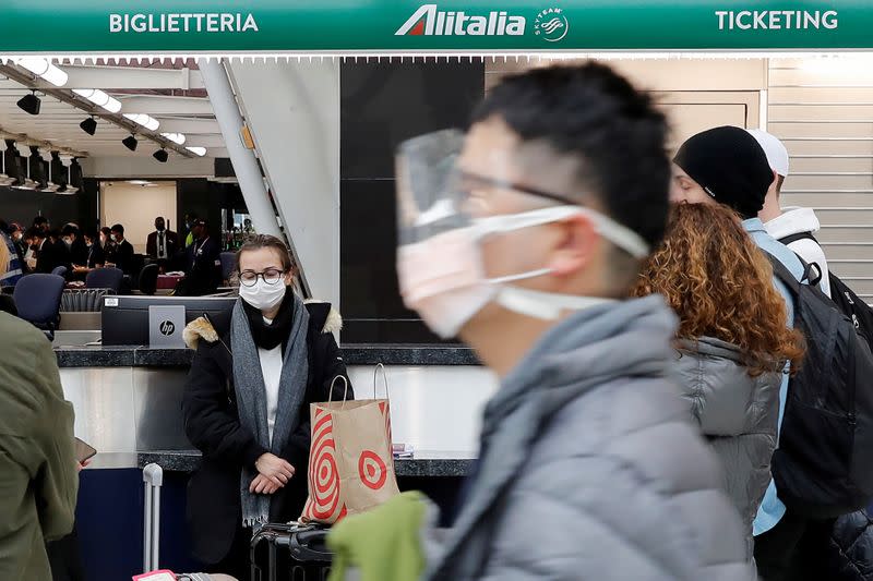 FILE PHOTO: A woman wearing a face mask waits with other passengers at the check-in area for an Alitalia, after further cases of coronavirus were confirmed in New York, at JFK International Airport in New York