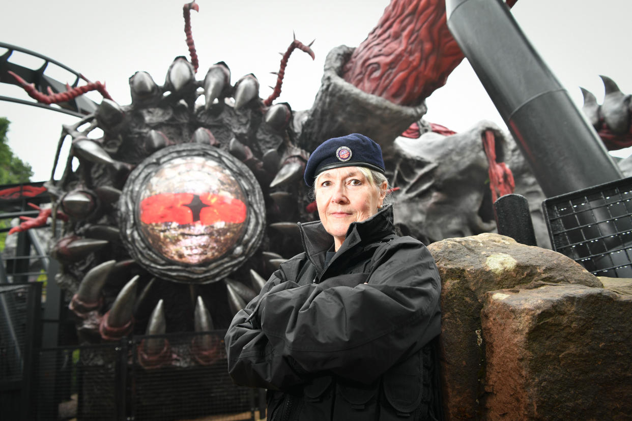 Woman in military beret stands in front of the Nemesis Reborn rollercoaster |