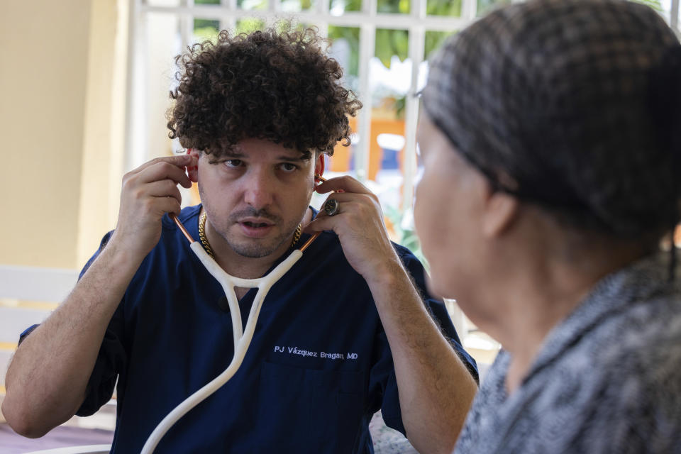 El Dr. Pedro Juan Vázquez, conocido por su nombre artístico PJ Sin Suela, atiende a un paciente en Loiza, Puerto Rico, el sábado 25 de mayo de 2024. El médico de 34 años viaja desde la capital de San Juan hasta el sur de la isla. y regiones centrales para atender a las comunidades que luchan tras los huracanes. Después de colgar su bata de médico, Vázquez dedica su tiempo a producir nueva música que hable de los problemas de la isla. (Foto AP/Alejandro Granadillo)