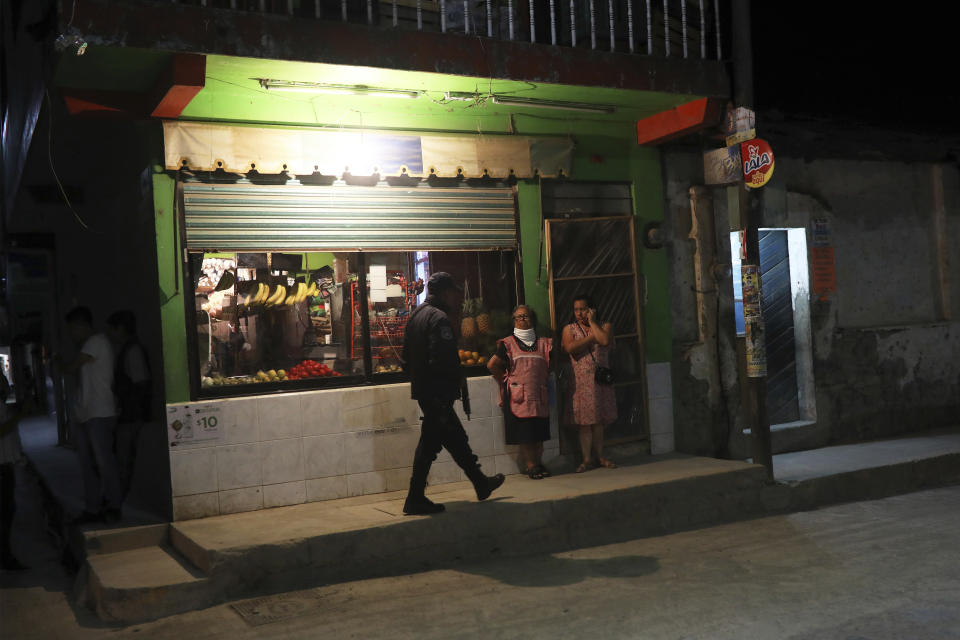 An armed policeman walks past a shop as residents watch the arrival of the hearse carrying the body of Maricela Vallejo, the slain 27-year-old mayor of Mixtla de Altamirano, before her wake in Zongolica, Veracruz state, Mexico, Thursday, April 25, 2019. Vallejo, her husband, and a driver were assassinated Thursday by multiple gunmen as they drove along a highway. (AP Photo/Felix Marquez)