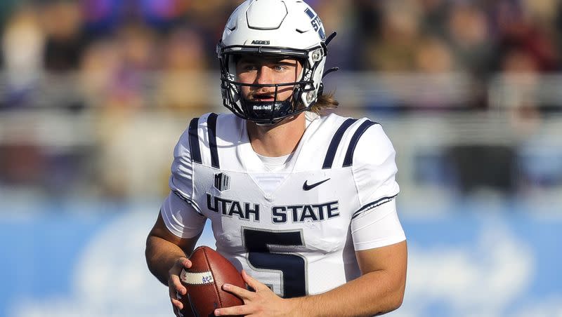 Utah State quarterback Cooper Legas (5) looks downfield as he scrambles with the ball against Boise State in the first half of an NCAA college football game, Friday, Nov. 25, 2022, in Boise, Idaho.