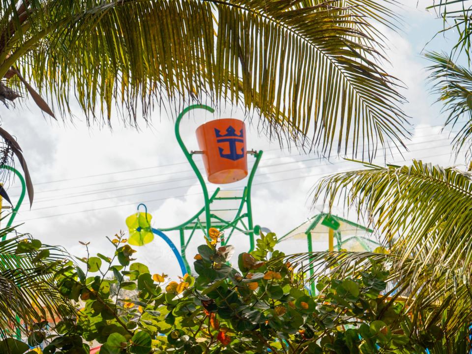 The top of the slashaway bay water playground is seen through shrubs and palm tree leaves on a cloudy day at CocoCay