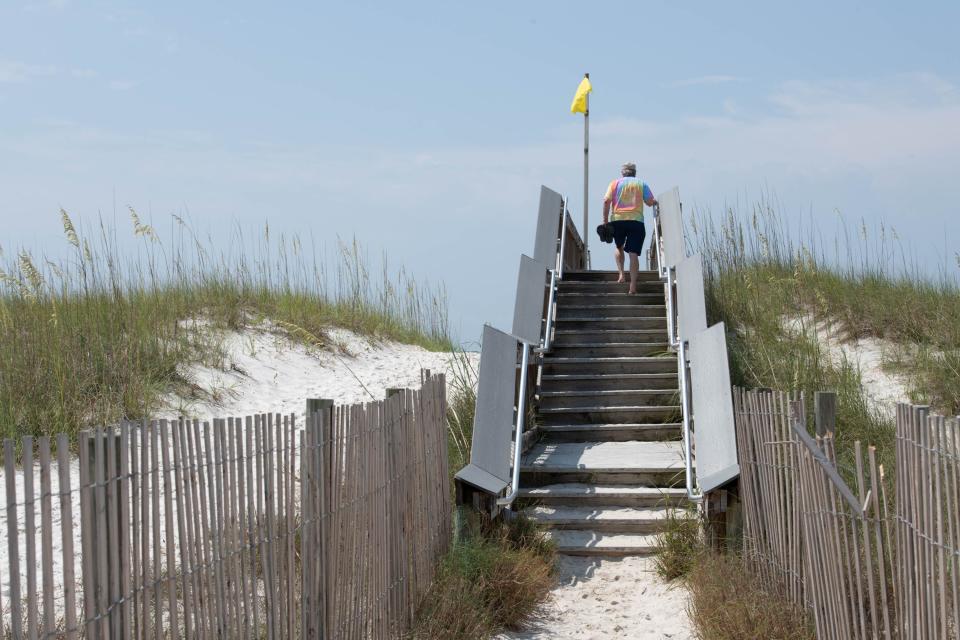 A man crosses over the dunes at Navarre Beach on Tuesday, July 11, 2023.