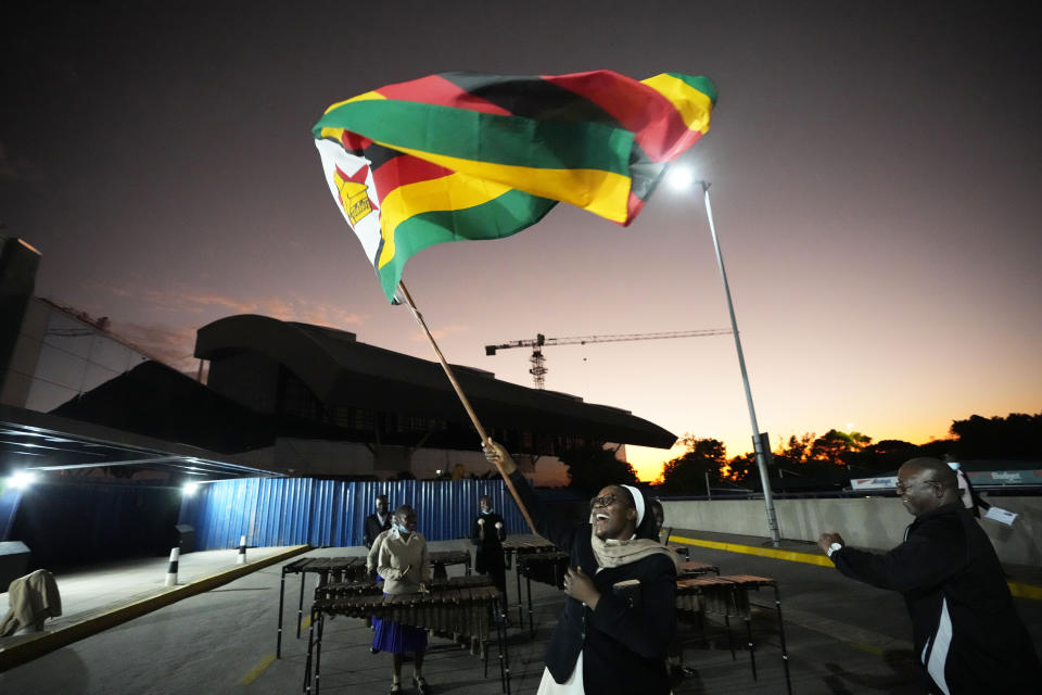 A nun celebrates while holding a Zimbabwean flag to welcome the Zimbabwean high school World and European moot court competition champions as they arrive back at the Robert Mugabe International airport in Harare, Thursday, July, 7, 2022. A history-making team of Zimbabwean high school students that became world and European moot court competition champions has been widely praised in a country where the education system is beset by poor funding, lack of materials and teachers’ strikes. (AP Photo/Tsvangirayi Mukwazhi)
