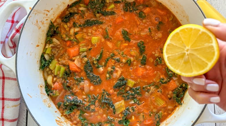 hand squeezing lemon juice into kale vegetable lentil soup pot