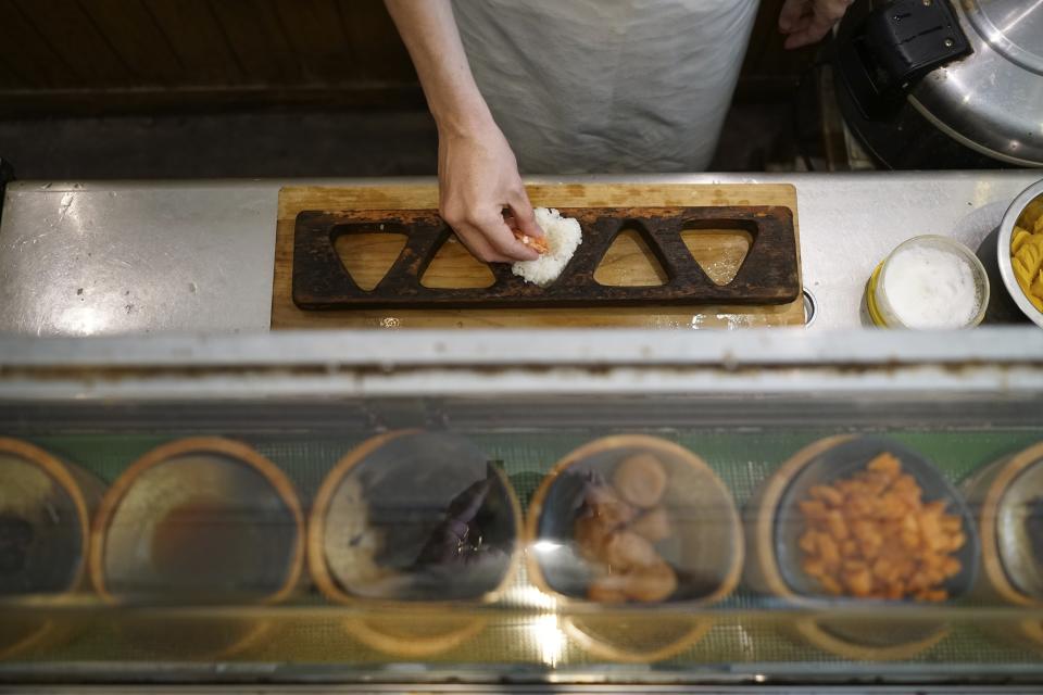 Yosuke Miura makes a rice ball with pieces of grilled salmon at Onigiri Asakusa Yadoroku, Tokyo's oldest onigiri restaurant, on June 3, 2024, in Tokyo. The word "onigiri" just became part of the Oxford English Dictionary this year. The humble sticky-rice ball, a mainstay of Japanese food, has entered the global lexicon. (AP Photo/Eugene Hoshiko)