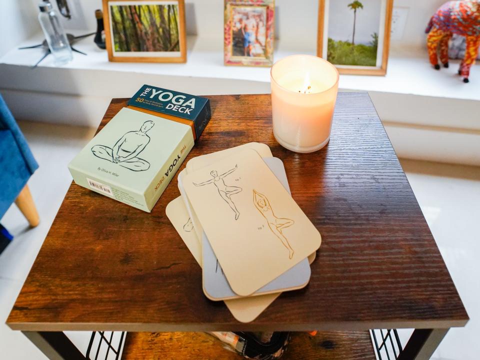 A brown, wooden table holds yoga cards and a white candle.