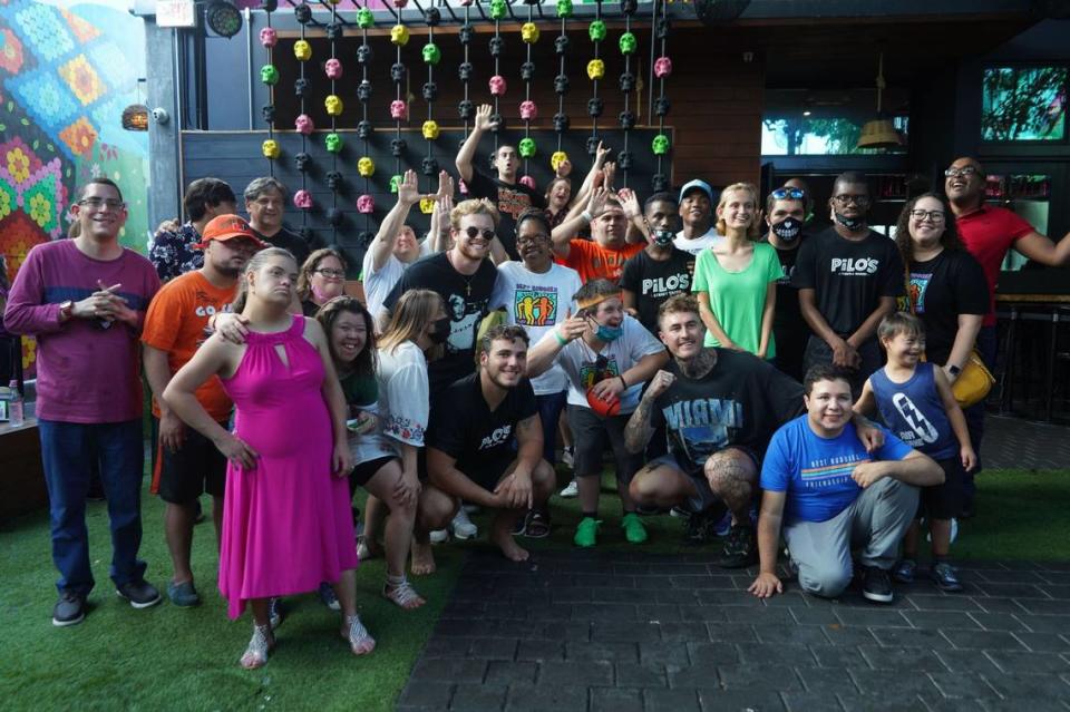 Miami Hurricanes quarterback D’Eriq King (standing with blue cap in last row) is shown on Tuesday, July 26, 2021, at Pilo’s in Miami during an NIL appearance by him and teammates Al Blades (not shown) and Ryan Ragone. Also appearing were Canes Lou Hedley and Clay James Under the guidance of attorney Adam Aranaout, they met and mingled with people with special needs who are supported in their efforts by the restaurant.