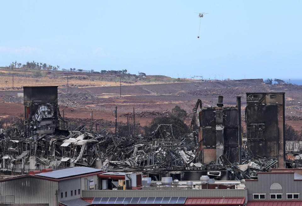 A firefighting helicopter flies near a building that was destroyed by a wildfire in Lahaina, Hawaii. / Credit: Getty Images