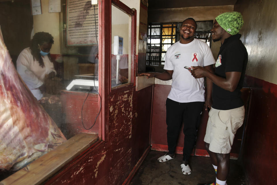 In this photo taken Thursday, June 11, 2020, gay Ugandan refugees Kasaali Brian, center, and Chris Wasswa, right, laugh while buying meat in Nairobi, Kenya. It is the only East African nation where someone can seek asylum and be registered as a refugee based on their LGBT status. Yet even in Kenya, they face discrimination and violence, and the country still criminalizes gay sex. (AP Photo/Brian Inganga)