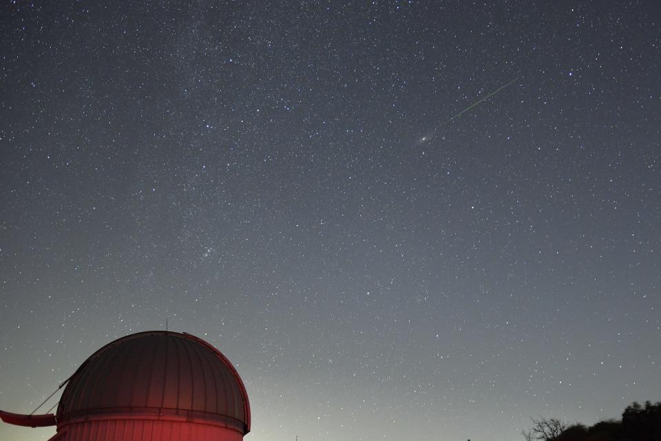 A meteor shower is pictured against a starry sky and picturesque foreground