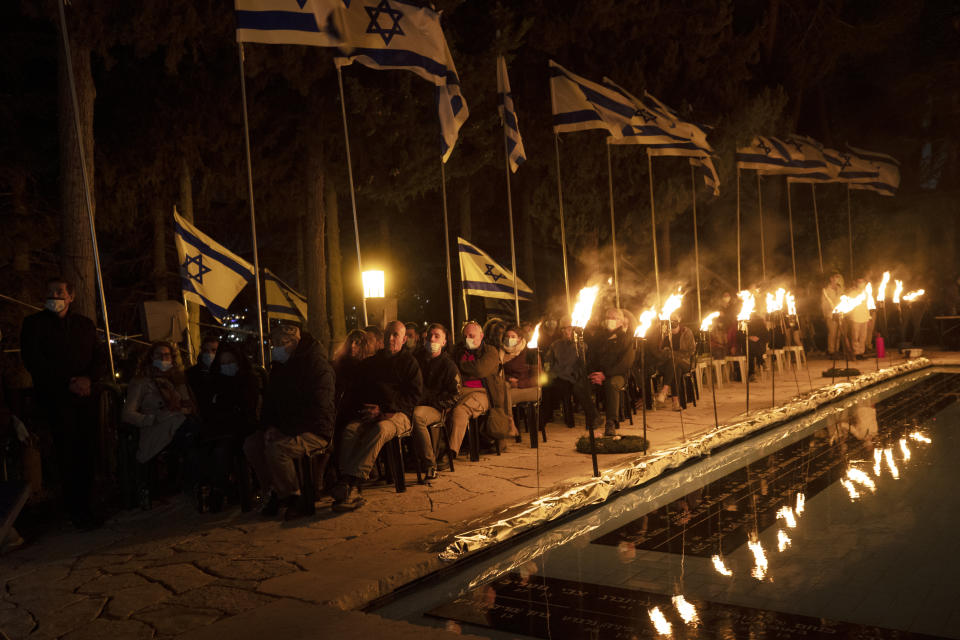 Guests are illuminated by torches during a Memorial Day ceremony commemorating fallen soldiers, at the military cemetery at Mount Herzl in Jerusalem, Tuesday, April 13, 2021. (AP Photo/Maya Alleruzzo)