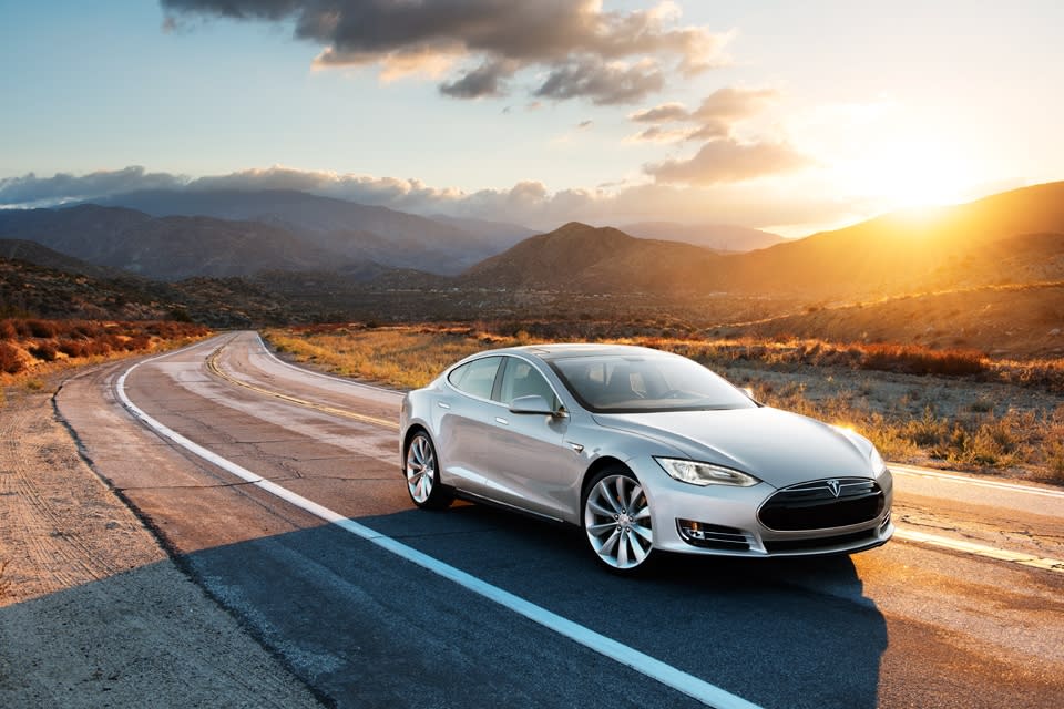 A silver Model S driving on a road, with hills in the background