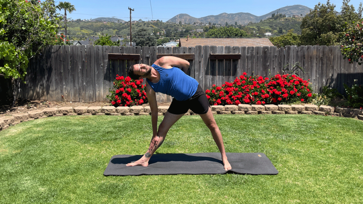 Man practicing yoga for tall people on a mat in his backyardd
