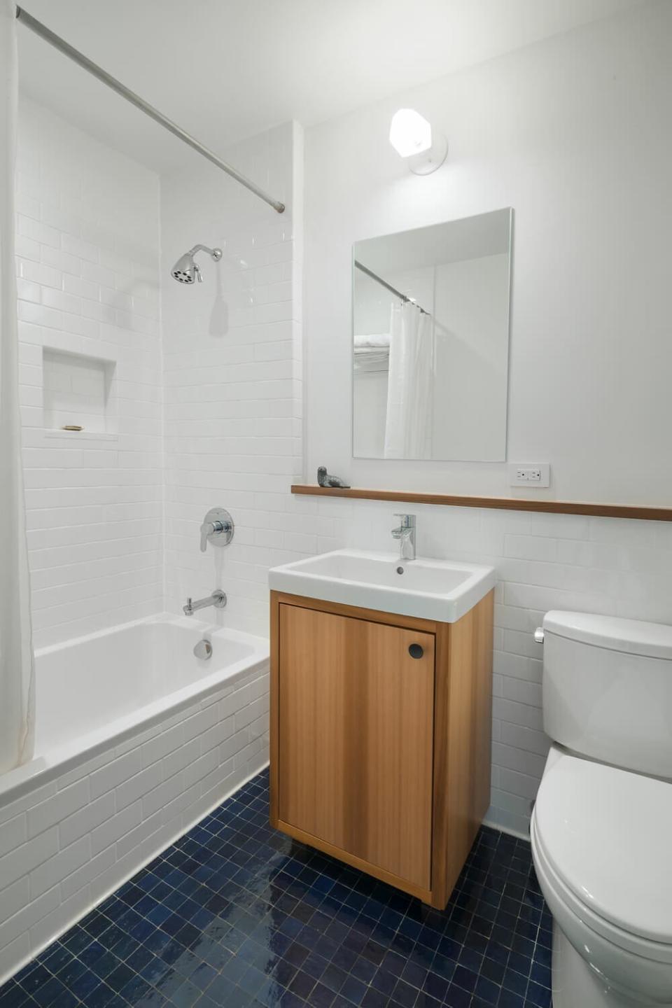 A white-and-blue bathroom with a built-in wooden shelf along the back wall.