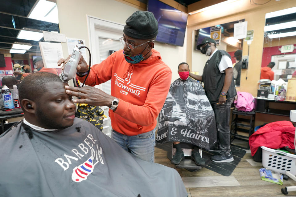 Kevin Fitzhugh, center left, cuts the hair of Mabreco Wright, left, as Wallace Wilson, right, cuts the hair of James McRae, Friday, April 9, 2021, in Hyattsville, Md. Barbers such as Fitzhugh and Wilson are members of the Health Advocates In Reach & Research (HAIR) program, which helps barbers and hair stylists to get certified to talk to community members about health. During the COVID-19 pandemic, a team of certified barbers have been providing factual information to customers about vaccines, a topic that historically has not been trusted by members of black communities because of the health abuse the race has endured over the years. (AP Photo/Julio Cortez)