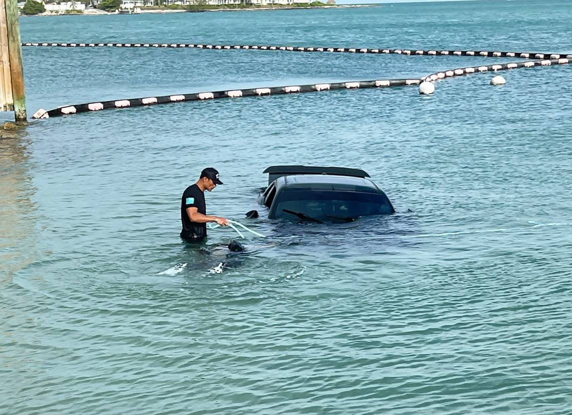 A Key West firefighter stands in the shallow water next to a sunken Dodge Challenger that police say a man drove into the ocean Sunday, April 28, 2024. Key West Police Department