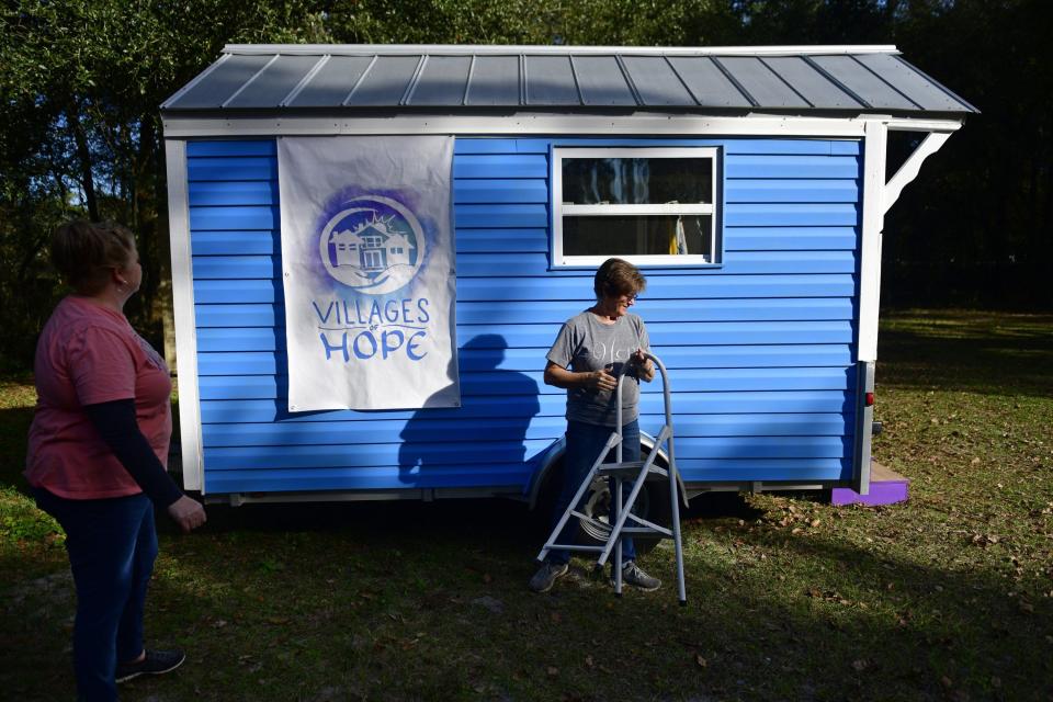 Carla Sweeney (left) and Donna Fenchel hang a sign on a promotional tiny home at their nonprofit, The Villages of Hope, a tiny-home community for sex-trafficking survivors.