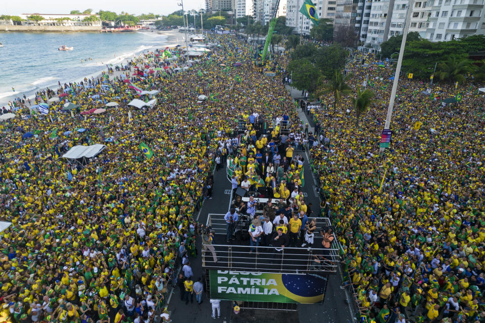 Brazil's President Jair Bolsonaro stands on a stage, adorned with a banner with a message that reads in Portuguese; "God, Country and Family," as he greets supporters gathered on Copacabana Beach during an Independence Day celebration, in Rio de Janeiro, Brazil, Wednesday, Sept. 7, 2022. Bolsonaro is waging an all-out campaign to shore up the crucial evangelical vote ahead of the Oct. 2 elections. (AP Photo/Rodrigo Abd)