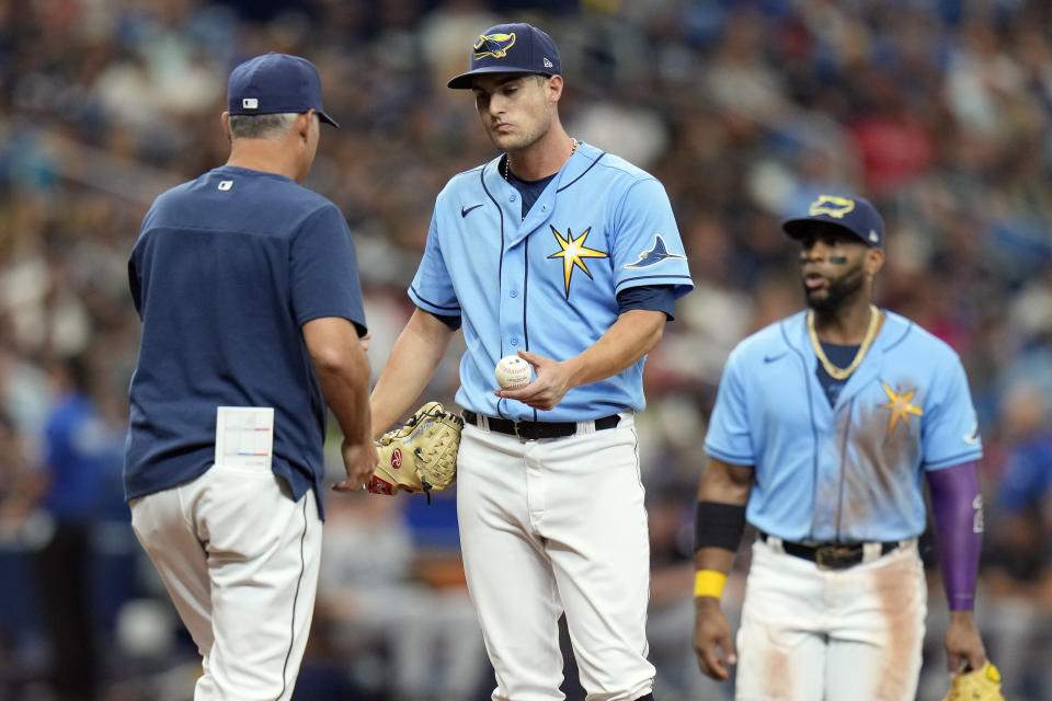 Tampa Bay Rays starting pitcher Shane McClanahan, center, hands the ball to manager Kevin Cash, left, as he is taken out of the game against the Cleveland Guardians during the fifth inning of a baseball game Sunday, July 31, 2022, in St. Petersburg, Fla. Looking on is third baseman Yandy Diaz. (AP Photo/Chris O'Meara)