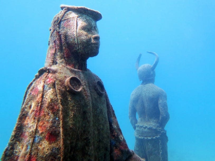 Two underwater sculptures covered in coral.