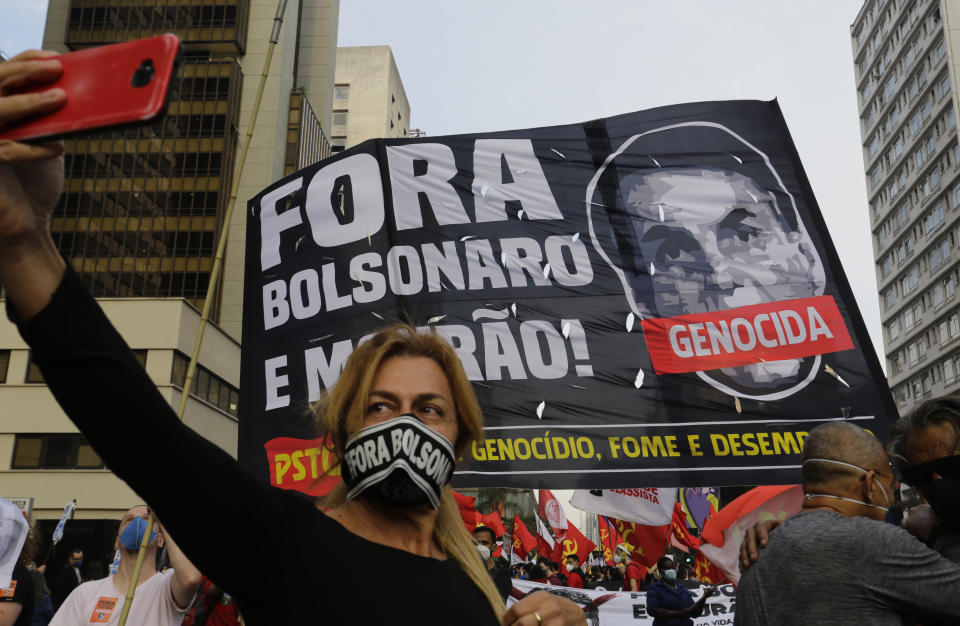 A woman takes a selfie backdropped by a banner depicting Brazilian President Jair Bolsonaro and a message that reads in Portuguese, "Get out Bolsonaro!" during a protest demanding Bolsonaro resign, in Sao Paulo, Brazil, Saturday, July 3, 2021. Activists called for nationwide demonstrations against Bolsonaro, gathering protestors to demand his impeachment amid allegations of potential corruption in the Health Ministry’s purchase of COVID-19 vaccines. (AP Photo/Nelson Antoine)