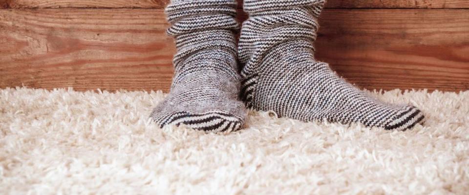 Legs of a woman in gray socks on the carpet on the wooden background. Vintage toning