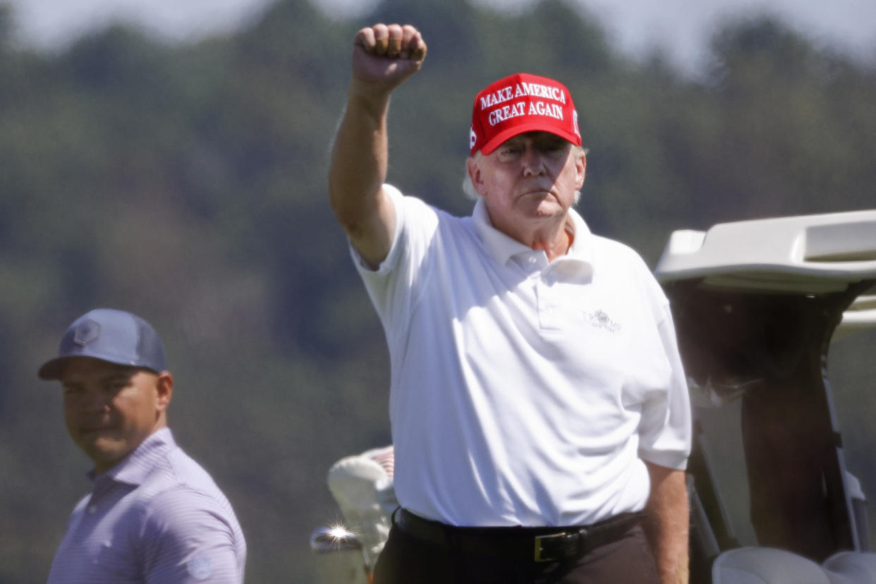 Donald Trump raises his fist while wearing a white polo shirt and a red Make America Great Again cap.