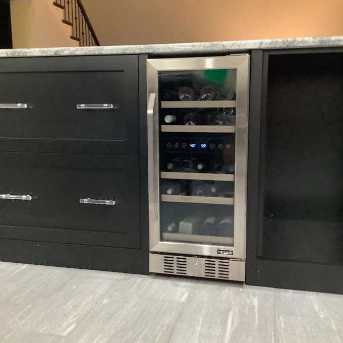 Built-in wine cooler with glass door partially filled with bottles, integrated with black cabinetry under a countertop