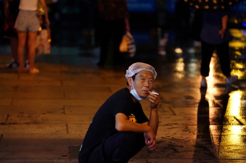 FILE PHOTO: Man smokes with a mask on his chin following the coronavirus disease (COVID-19) outbreak, during a rainfall in Beijing