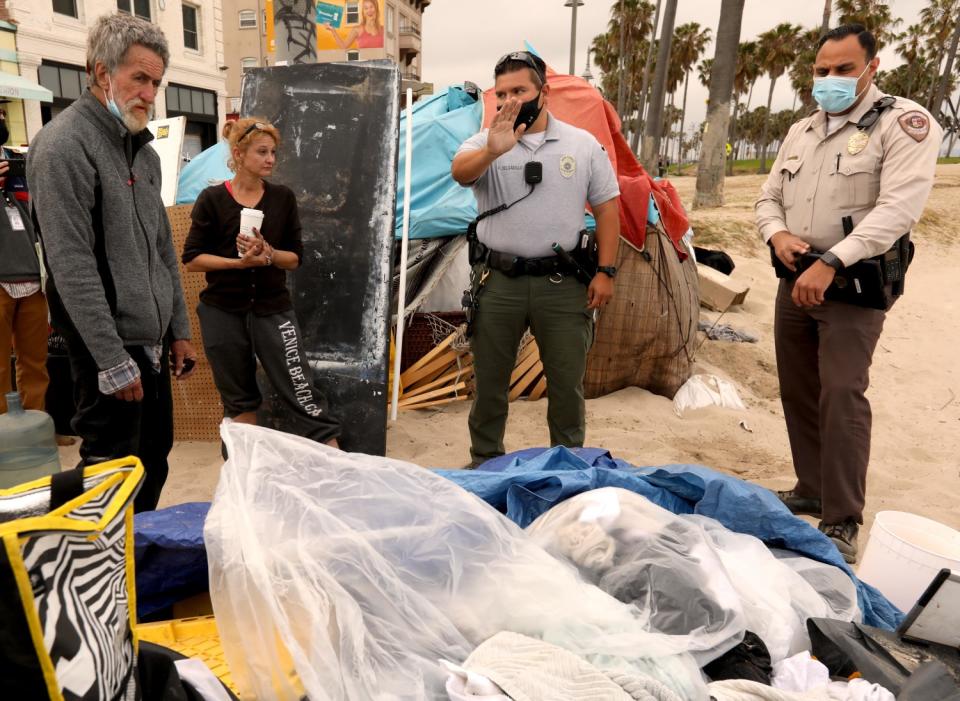 Two homeless people speak to security officers at their camp