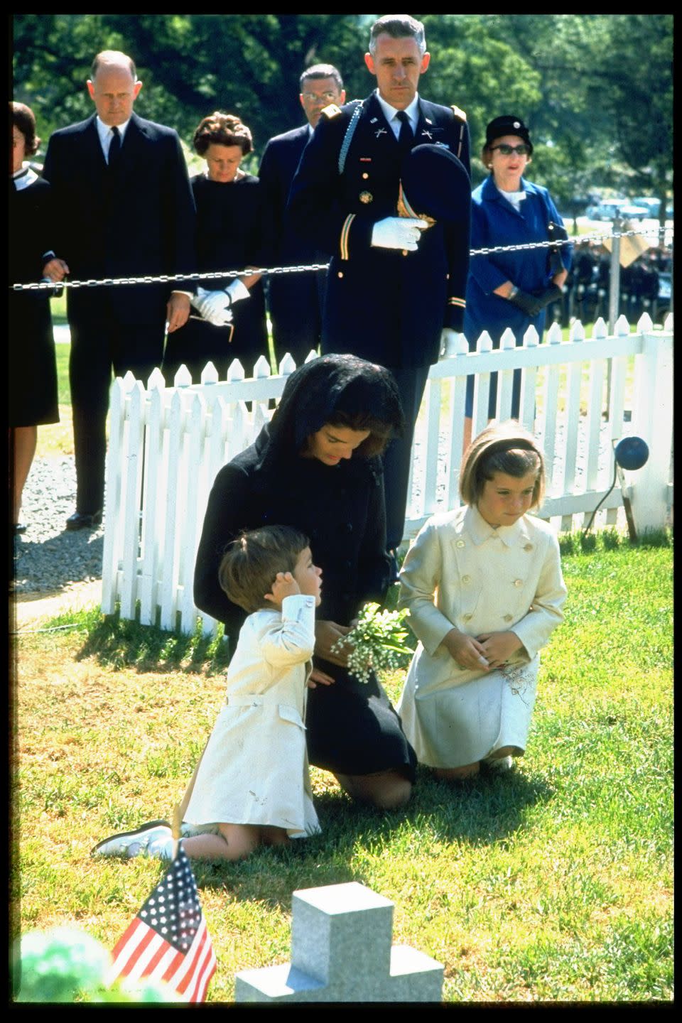 <p>Jacqueline Kennedy with her children John Jr. (left) and Caroline (right) kneel in prayer at the gravesite of President Kennedy, on his first birthday after his assassination. Pictured in the background are United States Army officer Maxwell Taylor, US Secretary of Defense Robert McNamara, and Treasury Secretary Douglas Dillon.</p>