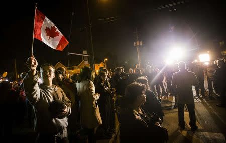 A man holds a Canadian flag after a hearse carrying the remains of Corporal Nathan Cirillo arrived at a funeral home in Hamilton, October 24, 2014. REUTERS/Mark Blinch