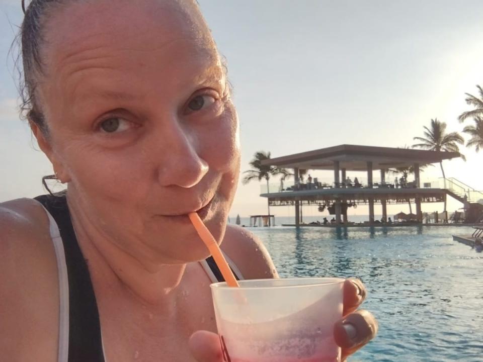 A woman taking a selfie while drinking a cocktail in a pool in a tropical place.
