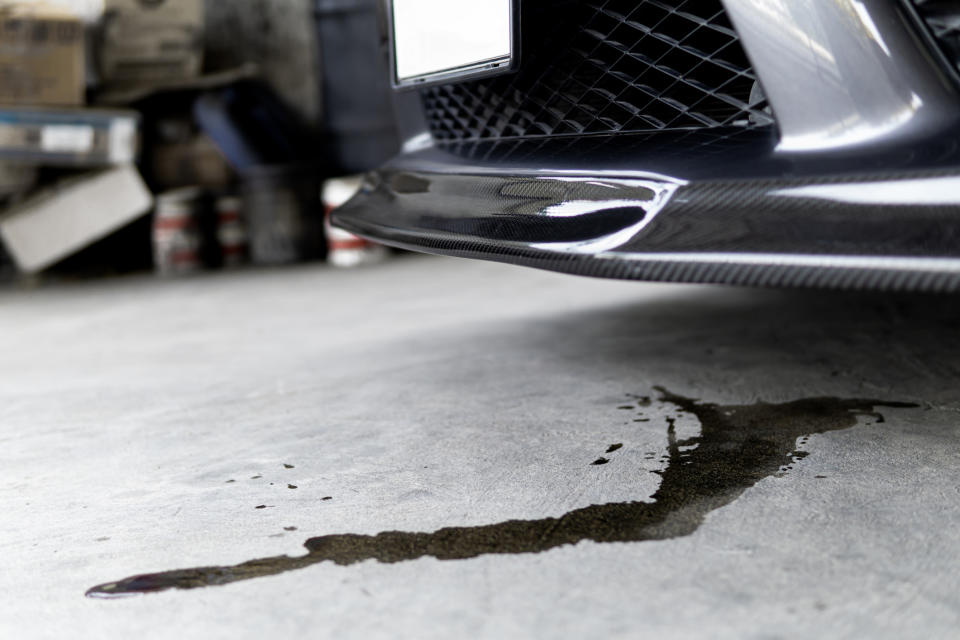 Close-up of a vehicle's front with oil leaking onto a concrete floor