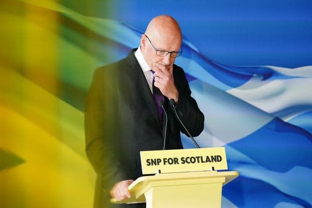 John Swinney, with head down, standing at an SNP lectern