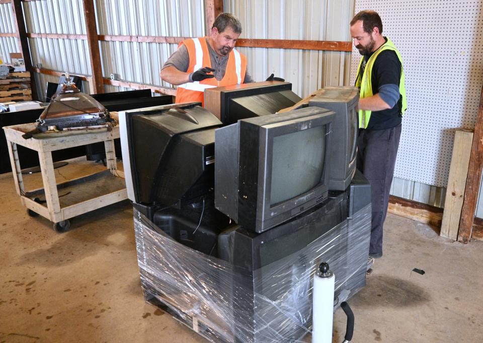 Steve Noble, environmental quality specialist with the Michigan Department of Environment, Great Lakes and Energy, and Jeff Buterbaugh wrap up a pallet of TVs hazardous because of lead glass tubes.