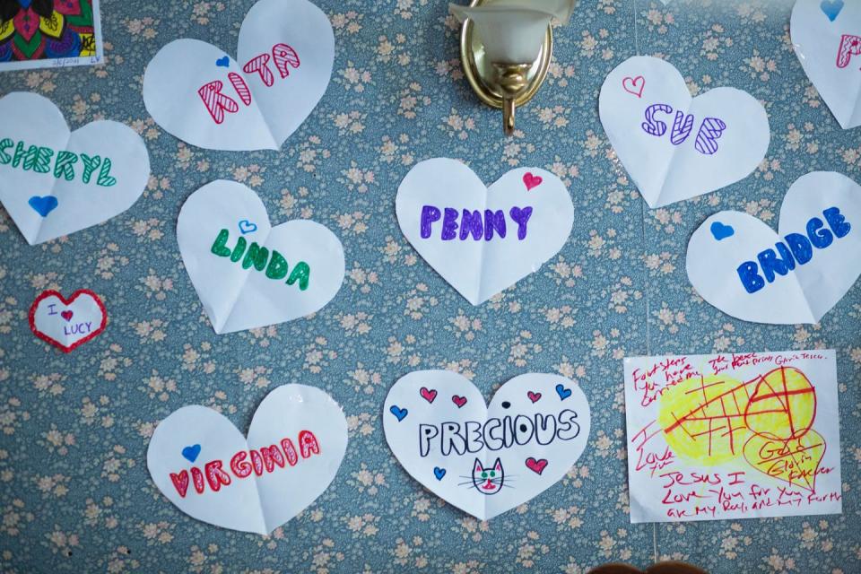 Paper hearts with women's names on them on a flowery bulletin board.