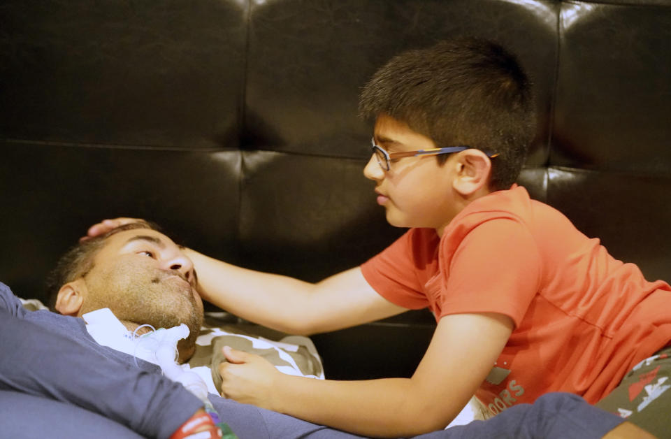 Ronan Kotiya, 11, right, touches his father Rupesh Kotiya after he helped him get ready for bed at their home in Plano, Texas, Friday, April 8, 2022. Ronan helps care for his father who suffers from ALS. Millions of Americans with serious health problems depend on children ages 18 and younger to provide some or all of their care at home. An exact number is hard to pin down, but researchers think millions of children are involved in caregiving in the U.S. (AP Photo/LM Otero)