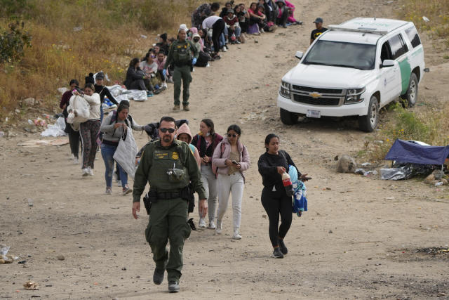 A U.S. Border Patrol agent leads a line of women to a van as they wait to apply for asylum between two border walls Thursday, May 11, 2023, in San Diego. Many of the hundreds of migrants between the walls that separate Tijuana, Mexico, with San Diego have been waiting for days to apply for asylum. Pandemic-related U.S. asylum restrictions, known as Title 42, are to expire May 11. (AP Photo/Gregory Bull)