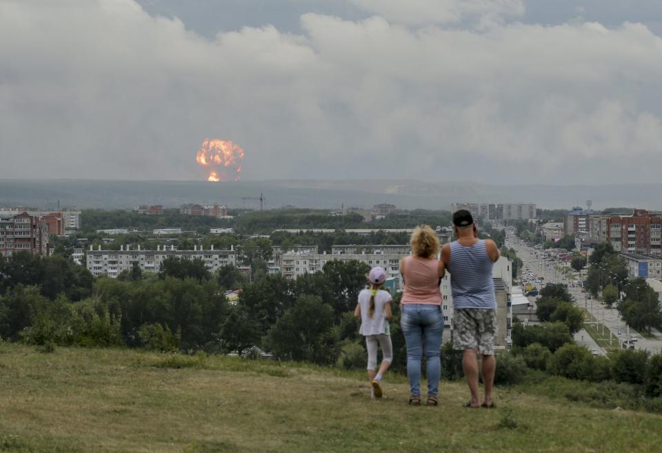 In this photo taken on Monday, Aug. 5, 2019, a family watches explosions at a military ammunition depot near the city of Achinsk in eastern Siberia's Krasnoyarsk region, in Achinsk, Russia.  Russian officials say powerful explosions at a military depot in Siberia left 12 people injured and one missing and forced over 16,500 people to leave their homes. (AP Photo/Dmitry Dub)