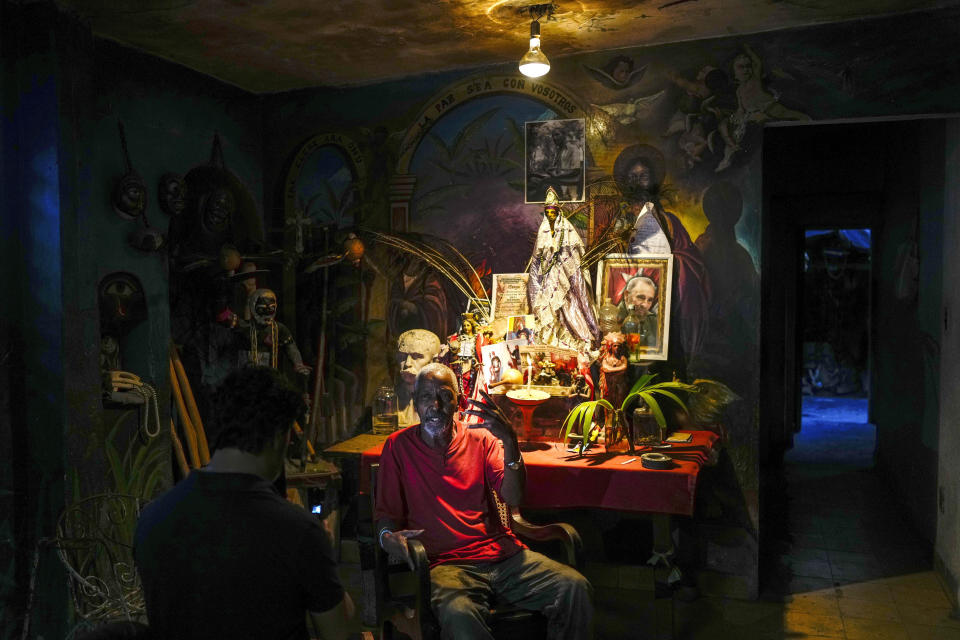 Juan González habla al lado de su altar con adornos de santería y católicos, además de una foto de Fidel Castro, el 10 de febrero de 2024, en su hogar en El Cobre, Cuba. En viviendas cubanas se pueden hallar creencias diversas, con altares, figuras de la Virgen María, estatuillas de Buda e imágenes de espíritus guerreros afrocubanos. (Foto AP/Ramón Espinosa)