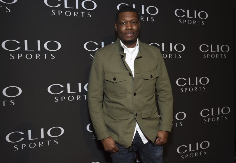 A man posing in a green shirt and jeans against a black backdrop