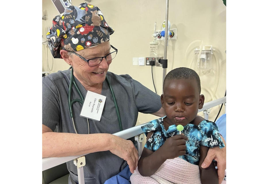 Nurse Ellen Reynolds of Children’s Surgery International gives a lollipop to patient Ategeka, whose last name they are keeping confidential to protect his privacy, in a bed at Holy Innocents Children's Hospital in Mbarara, Uganda on Feb. 2, 2024. Ategeka is wearing a Harry Potter-themed gown made by Giuliana Demma, a New Jersey girl who, with her sister Audrina, have sewn and donated 1,800 brightly colored, kid-themed hospital gowns to sick children across the U.S. and Africa. (Amy Smith/Children's Surgery International via AP)